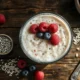 Overhead shot of a wooden table with a large glass bowl of oatmeal topped with fresh blueberries, ra