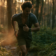 Läufer joggt in lockerem Tempo auf einem Waldweg und schaut auf seine Pulsuhr am Handgelenk
