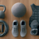 ** Hyrox-Heimausrüstung: Kettlebell, Medizinball, Springseil und Laufschuhe nebeneinander auf dem Boden