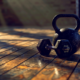 Kettlebell und Kurzhantel nebeneinander auf dem Boden eines Home Gyms, der versetzte Schwerpunkt der Kettlebell im Vergleich zur ausbalancierten Hantel