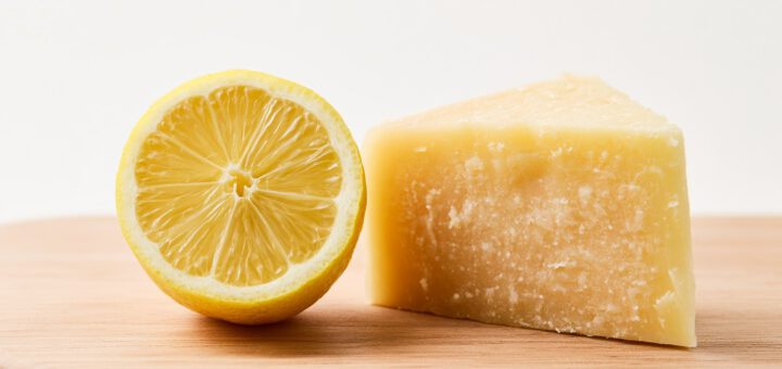 Zitrone neben einem Stück Hartkäse auf einem hellen Küchenbrett