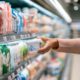 Hand greift im Kühlregal des Supermarkts nach einem Becher Magerquark