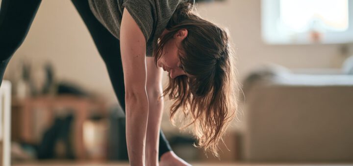 Frau dehnt die Beinrückseite in einer Vorbeuge im Wohnzimmer