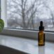 Vitamin-D-Tropfen in einer braunen Pipettenflasche auf der Fensterbank, draußen kahle Bäume im Winterlicht