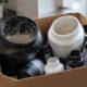 Karton mit aussortierten Supplements: angebrochene Proteindosen, Kapselflaschen und ein Shaker