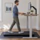 Mann geht im Homeoffice auf einem flachen Walking Pad am Steh-Schreibtisch, Unterarme waagerecht auf Ellbogenhöhe